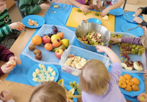 Dzieci z grupy Niebieskie rozdzielają i kroją owoce, pokrojone wrzucają do dużej miski.