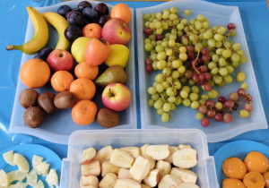 Na stole ułożone są w pojemnikach i na talerzach składniki - owoce na sałatkę.