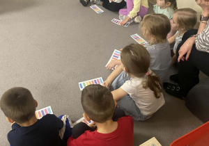 Dzieci siedzą w kole, przed nimi rozłożone są podpisane paski z kolorową klawiaturą w gamie C-dur