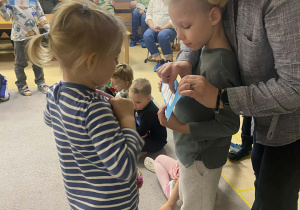 Dziewczynka wskazuje i odczytuje zdanie obrazkowo-wyrazowe pokazywane przez chłopca, zapisanego na pasku z kartonu.