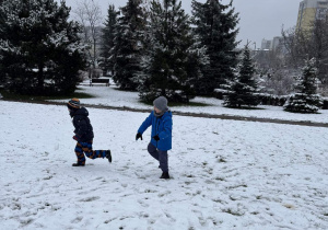 Chłopiec goni drugiego chłopca próbując trafić go kulką śnieżką