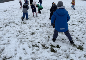 Dzieci biegają po górce pokrytej śniegiem.