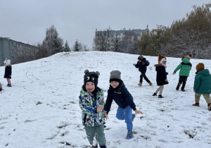 Dzieci gonią się na górce pokrytej śniegiem.
