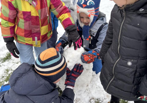 Dzieci przyglądają się swojej śniegowej budowli bałwana.