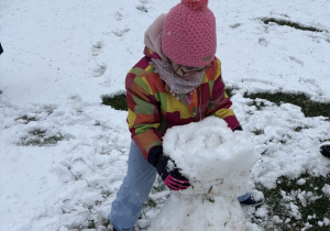 Dziewczynka układa jedną na drugiej kulę śniegową.