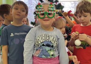 Dzieci pozuję na tle choinki, dziewczynka ma świąteczne okulary