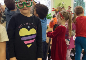 Dzieci ubierają choinkę, dziewczynka pozuje w okularach z choinką