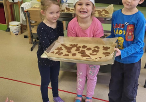 Dzieci trzymają wykrojone ciastka - pierniki na blaszce do pieczenia