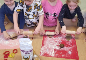 Dziewczynki i chłopcy wałkują ciasto na pierniczki