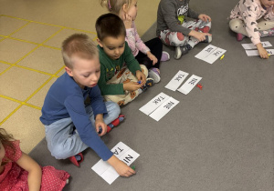 Dzieci siedzą w kole, przed nimi leżą ułożone dwa napisy wyrazów TAK, NIE