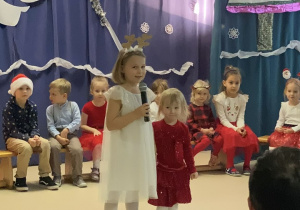 Dwie dziewczynki recytują wiersze, w tle dzieci siedzą na ławeczce.