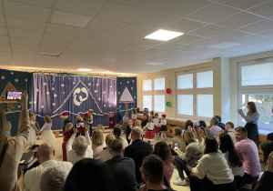 Dzieci z grupy Niebieskiej tańczą w parach na sali gimnastycznej na tle świątecznej dekoracji