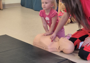 Dziewczynka z pomocą pani ratownik ćwiczy udzielanie pierwszej pomocy.