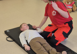 Chłopiec leży na materacu, obok pani ratownik.