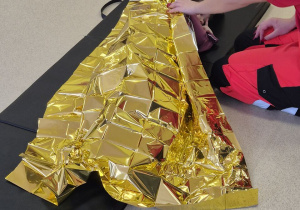 Na materacu leży dziecko przykryte kocem termicznym.