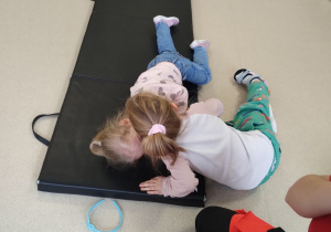 Jedna dziewczynka nachyla się nad kożenanką i uczy się sprawdzać, czy jest słyszalny oddech