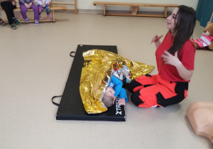 Pani ratowniczka medyczna demonstruje dzieciom działanie koca termicznego