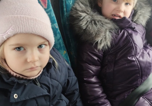 Dwie dziewczynki siedzą a autokarze przypięte pasami