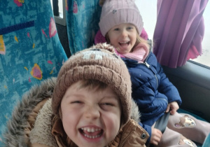 Dzieci z grupy niebieskiej siedzą w autokarze czakając na podróż do teatru, dziewczynka i chłopiec uśmiechają się