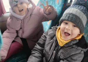 Dziewczynka i chłopiec siedzą w autokarze, mają zadowolone miny