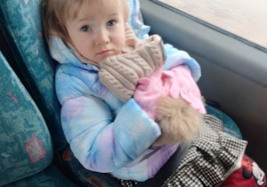 Dziewczynka siedzi w autokarze, ściska czapkę w ręku