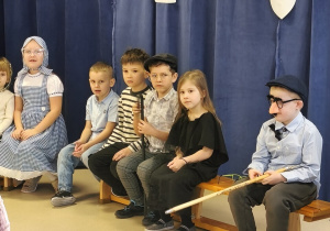 Na ławeczce siedzi sześcioro dzieci. Dwóch chłopców jest przebranych za dziadka, a jedna z dziewczynek za babcię.