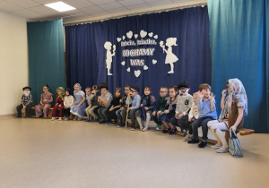 Cała grupa siedzi na ławeczce. Dzieci przebrane są za babcie i dziadków.