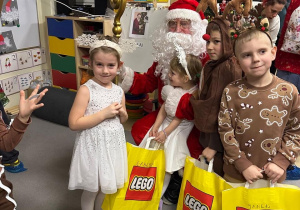 Dziewczynka i chłopiec stoją obok Mikołaja, trzymają prezenty, które otrzymały (2)