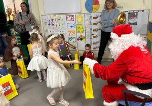 Dziewczynka podchodzi do Mikołaja, który wręcza jej prezent