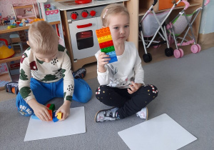 Dziewczynka prezentuje swoją budowlę z klocków, chłopiec obok tworzy budowlę