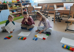 Dziewczynka układa klocki w odpowiednim miejscu na podkładce według słownej instrukcji nauczyciela