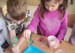 Dzieci nalewają pipetą wodę z barwnikiem na kostkę lodu