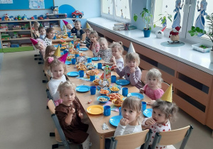 Dzieci siedzą przy długim stole z poczęstunkiem