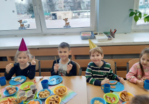Kilkoro dzieci siedzi przy stole z poczęstunkiem