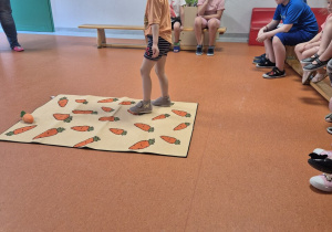 Dziewczynka przechodzi na drugi koniec maty stawiając stopy na nadrukowanych marchewkach.