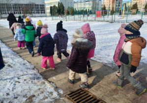 Dzieci z grupy Niebieskiej spacerują w parach obok budynku przedszkola
