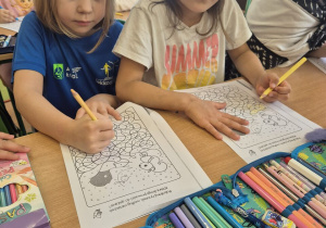 Dwie dziewczynki siedzą w ławce i wykonują zadanie na karcie pracy