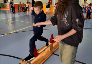 Chłopiec przechodzi po ławeczce pokonując tor przeszkód z pomocą starszej uczennicy