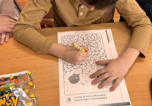 Chłopiec siedzi w szkolnej ławce i koloruje obrazek.