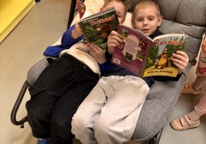 Chłopcy wspólnie siedzą na fotelu i czytają wybrane przez siebie książki.