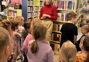 Dzieci słuchają pani bibliotekarki opowiadającej o książkach znajdujących się w bibliotece.