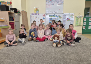 Grupa dzieci siedzi na dywanie z Misiem Insulisiem