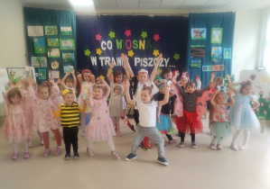 Dzieci z grupy niebieskiej pozują w strojach balowych na tle dekoracji wiosennej.