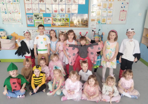 Dzieci z grupy niebieskiej pozują w strojach balowych w sali przedszkolnej na tle tablicy daltońskiej.