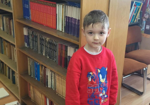 Chłopiec stoi przy regale z książkami