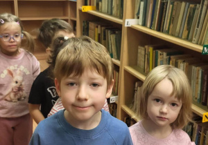 Dzieci stoją w bibliotece przy regale