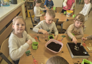 Dzieci nakładają ziemię do swoich doniczek.