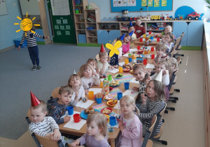 Dzieci siedzą przy długim stole z poczęstunkiem