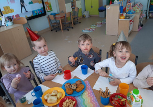 Dzieci siedzą przy stole i jedzą przekąski