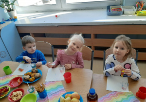 Troje dzieci siedzi przy stole i je galaretki